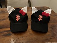 Front view of both identical black Hello Kitty San Francisco Giants baseball caps showing logo, ears and bows