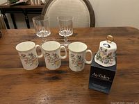 Full lot showing three floral mugs, Aynsley bell on box, two crystal wine glasses