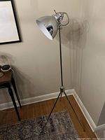 Full view of chrome spotlight floor lamp on tripod base next to wall