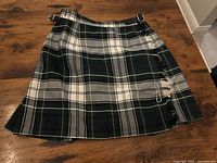 Full view of green, black and white tartan kilt with buckles and safety pin
