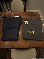 Folded navy Dickies pants with tag next to folded grey pants with tag on wooden table