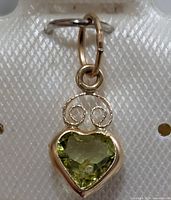 Front view of earring showing heart-shaped peridot, gold bezel and swirl accent