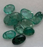 Close-up of nine loose emeralds showing color range and inclusions