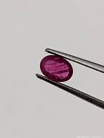 Close-up of loose oval faceted ruby held by tweezers