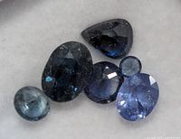 Close-up of six faceted blue sapphire stones on white background