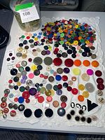 Overview of entire assortment of buttons laid out on fabric, plastic container visible