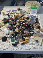 Overview of button assortment spread on cloth with metal tin