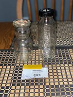 Two vintage glass bottles: baby bottle with black cap and rubber nipple inside, and mini creamer bottle with paper lid