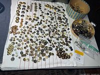 Full layout of hundreds of metal buttons on cloth and in tub