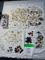 Overview of entire collection spread on white cloth, showing large quantity of white shell buttons and grouped coloured buttons