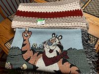 Folded crocheted afghan atop folded Tony the Tiger woven throw