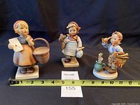 Front view of three Hummel figurines with tape measure
