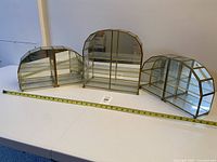 Front view showing three of the brass and glass display cabinets with measuring tape for scale