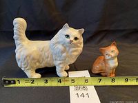 Front view of both Beswick cat figurines beside tape for length