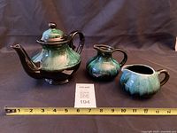 Front view of teapot with lid flanked by two creamers, tape measure for scale