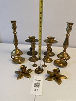 Group view of all eleven brass candle holders with measuring tape for scale