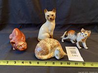 Front view of all four cat figurines with ruler for scale