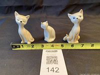Three cat figurines side by side with tape measure for length reference