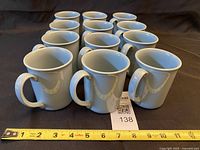 Front angled view showing all 12 mugs with tape for scale