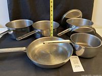 Front view of all five pans, two lids visible, measuring tape for scale