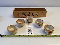 Front view of five sake cups arranged before wooden box