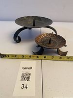 Two metal pricket candle holders side by side with tape measure for width reference