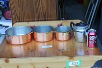 Three copper saucepans, teapot and scale can on wooden surface
