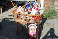 Overall view of wicker bassinet on stand filled with assorted dolls and boxed doll in front