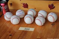 All eight autographed baseballs displayed on wooden surface with reference can for scale.
