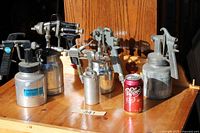 All five spray guns positioned on tabletop with reference soda can