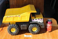 Full side view of yellow Tonka Mighty dump truck next to soda can for scale