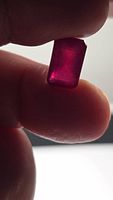 Rectangular ruby held between fingers, showing color and cut