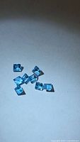 Cluster of eight square-cut blue gemstones on neutral background