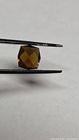 Hexagonal fancy cut tourmaline held by tweezers, face view shows deep orange color