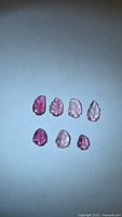 Seven pink leaf-cut tourmaline gemstones displayed on light background