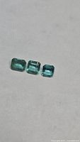 Three loose emeralds displayed on white surface