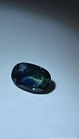Oblique view of the oval sapphire showing mixed blue-green tones and faceting.