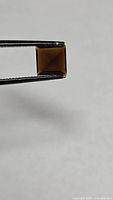 Square yellow-orange tourmaline held in tweezers, top view showing color and cut