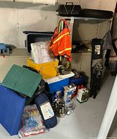 Overview of stacked camping gear: cooler, tarps, lanterns, safety vest, chairs, stove case visible