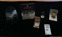 Group shot of all five items: Nikon binoculars, Rolls Razor set, silver pocket watch, gold pocket watch, brass compass