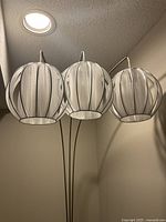 close view of three white fabric globe shades on silver arms