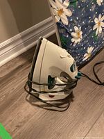 White and teal steam iron in black wire holder