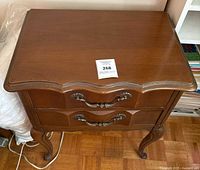 Front view of cherry two-drawer bedside table showing cabriole legs and brass-tone pulls