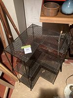 Front angled view of black perforated metal corner shelf showing four tiers and lattice pattern