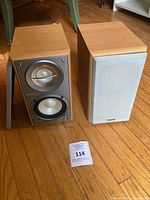 Both speakers shown, one with grille removed displaying drivers, paper lot card visible