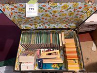 Open suitcase showing rows of green hardcovers, yellow-spine hardcovers, assorted paperbacks, floral lining