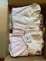Box containing folded white and pink lace baby dresses