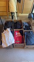 Overview of six boxes with clothing, hoodie, quilted jacket, bags visible