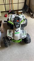 Front view of white and green ride-on ATV showing body, wheels, handlebars