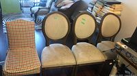 Four chairs: three beige oval-back, one plaid